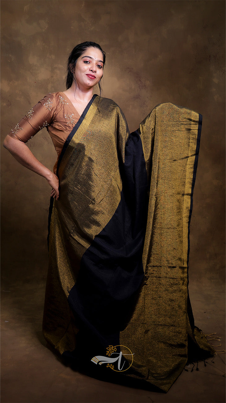 Woman wearing a traditional saree with a gold and black pattern against a brown background