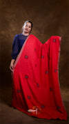 Woman holding a red saree with black patterns against a brown background