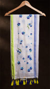 Scarf with floral patterns and tassels hanging on a wooden hanger against a dark background
