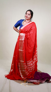 Woman wearing a red saree with a blue blouse against a plain background