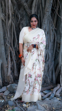 Woman in a floral saree standing in front of a large tree with thick trunk.