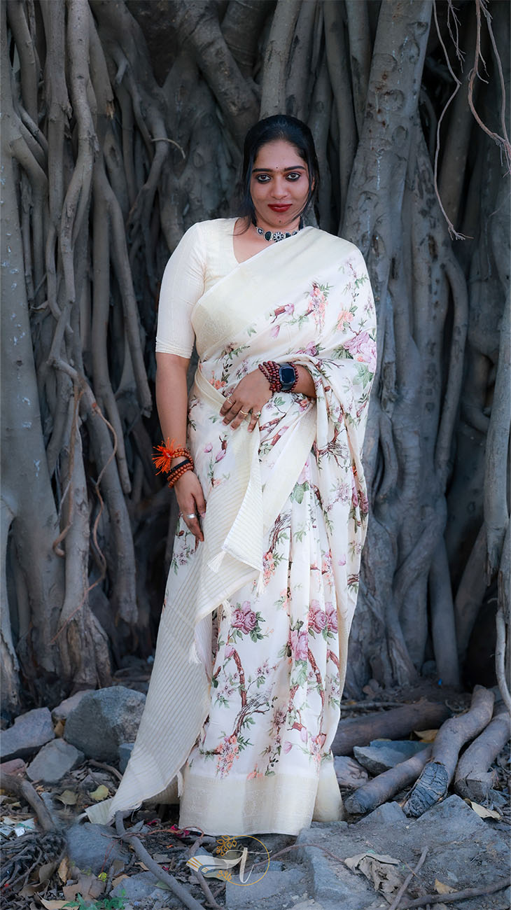 Woman in a floral saree standing in front of a large tree with thick trunk.