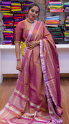 Woman wearing a traditional saree in a store setting with colorful fabrics in the background.