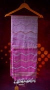 Pink patterned scarf with tassels hanging on a wooden hanger against a dark background with orange lights.