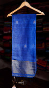 Blue saree with white patterns on a wooden hanger against a blurred fabric background