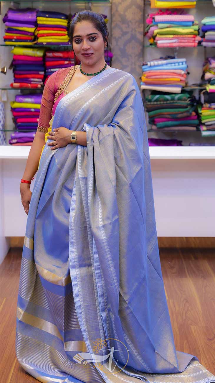 Woman wearing a blue saree with a colorful background of fabric.