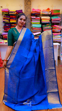 Woman holding a blue saree with a background of colorful fabric stacks