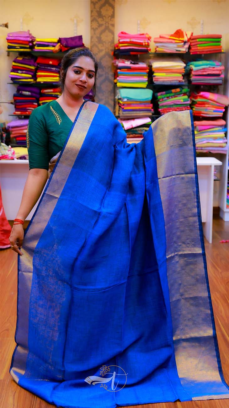Woman holding a blue saree with a background of colorful fabric stacks