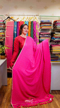 Woman holding a pink saree in a fabric store with colorful fabrics in the background.