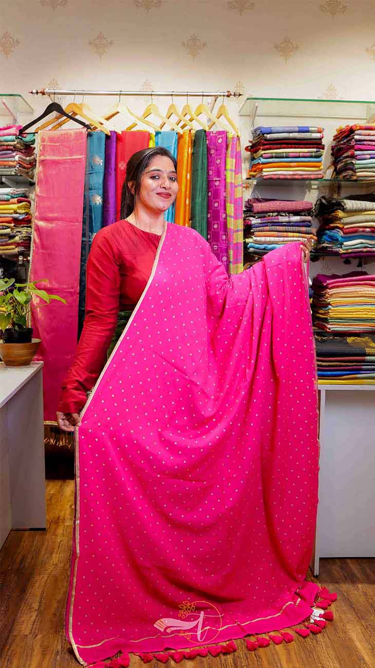 Woman holding a pink saree in a fabric store with colorful fabrics in the background.