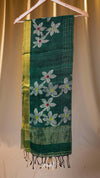 Green scarf with floral embroidery on a wooden hanger against a beige curtain background