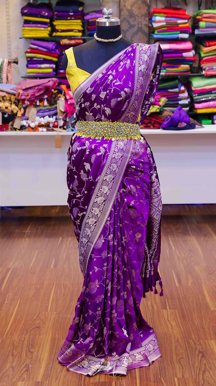 Purple saree with a yellow blouse on a mannequin against a colorful fabric background.