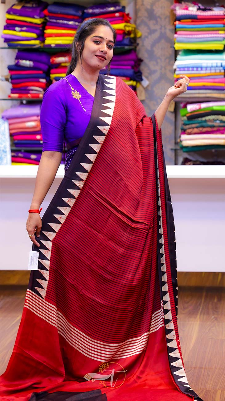 Woman wearing a red saree with a black border in a fabric store.