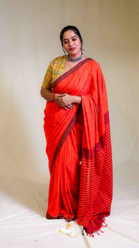Woman wearing a bright red saree with a gold border against a plain background