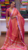 Woman wearing a pink saree with a colorful background of folded sarees.
