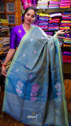Woman holding a blue saree with floral patterns in a fabric store.