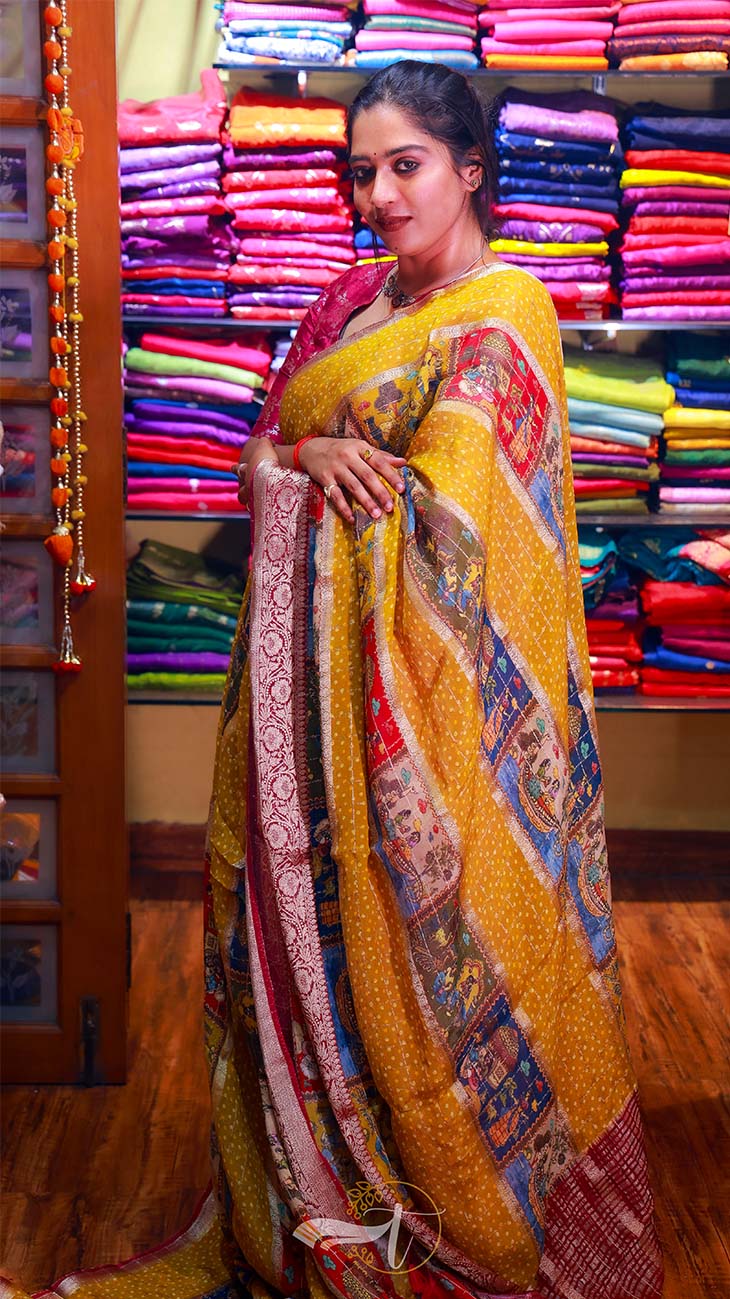 Woman in a yellow saree with a colorful pattern standing in front of a display of colorful fabrics.