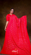 Woman wearing a red saree with a white grid pattern on a brown background