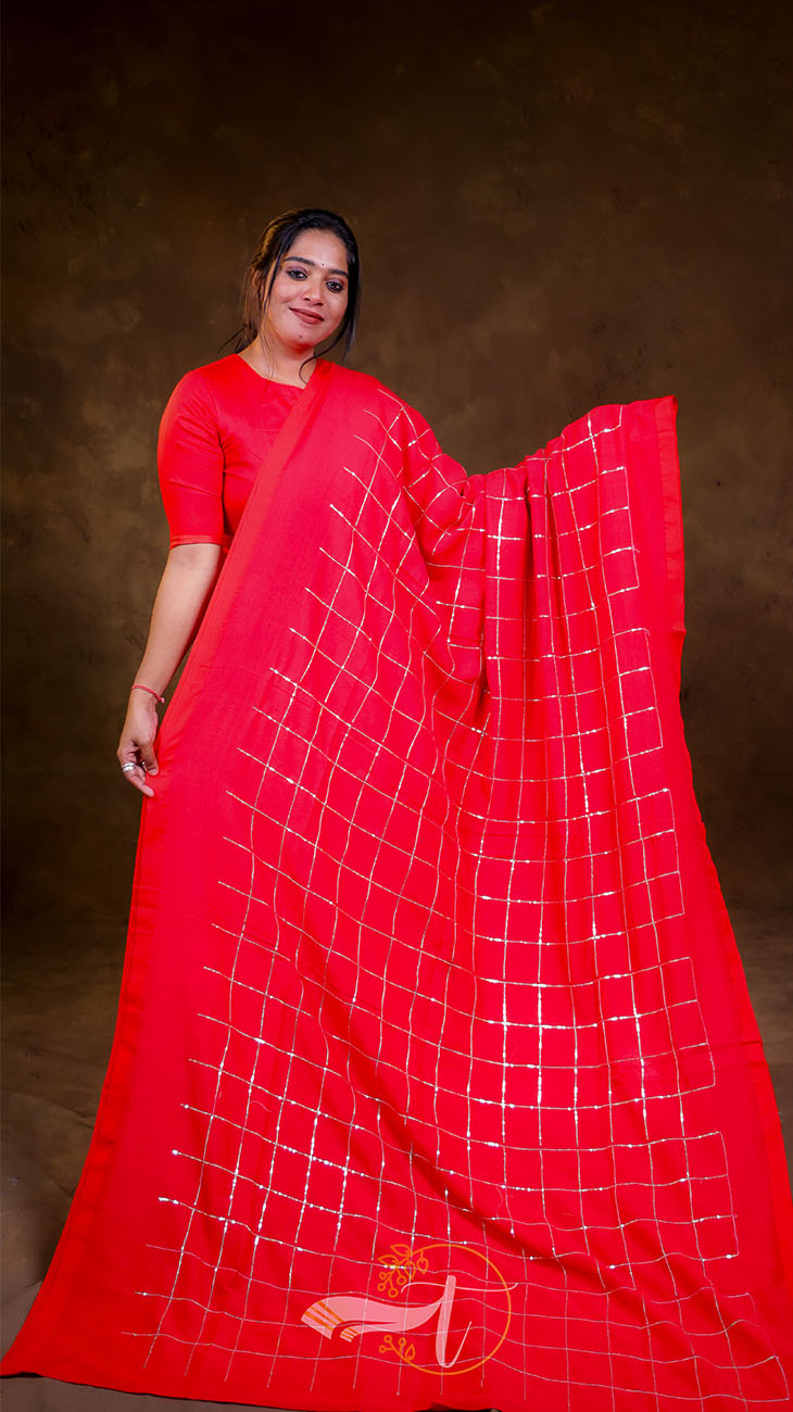 Woman wearing a red saree with a white grid pattern on a brown background