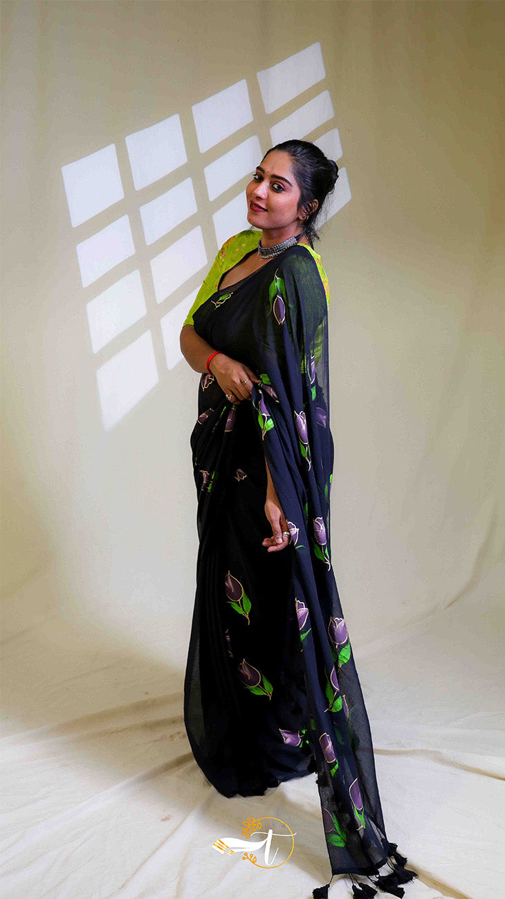 Woman wearing a black saree with floral patterns in a studio setting