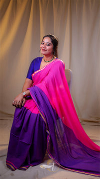 Woman wearing a pink and purple saree sitting against a plain background