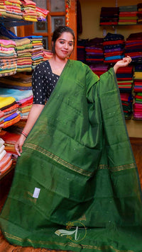 Woman holding a green saree in a fabric store with colorful fabrics in the background