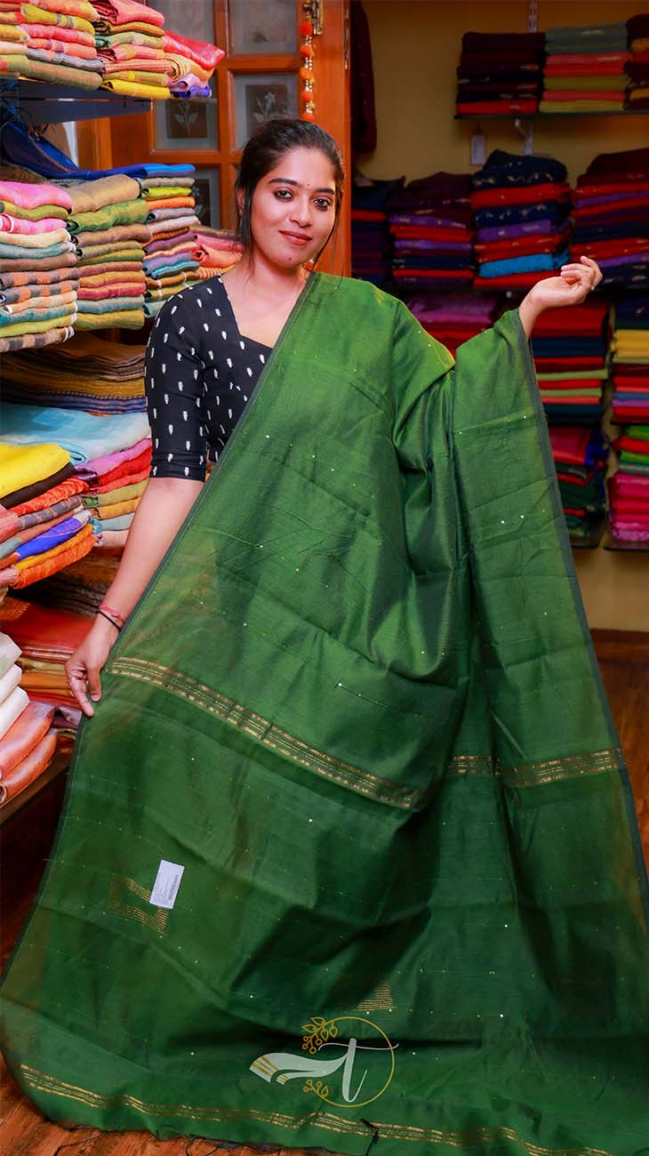 Woman holding a green saree in a fabric store with colorful fabrics in the background