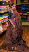 Woman in a brown saree standing in a fabric store with colorful fabrics in the background.