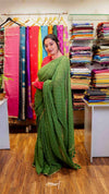 Woman wearing a green saree in a fabric store with colorful sarees on display.