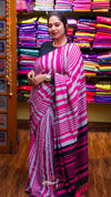 Woman wearing a pink and white striped saree in a colorful fabric store.