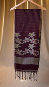 Dark purple scarf with floral patterns and fringes on a wooden hanger against a beige curtain background.