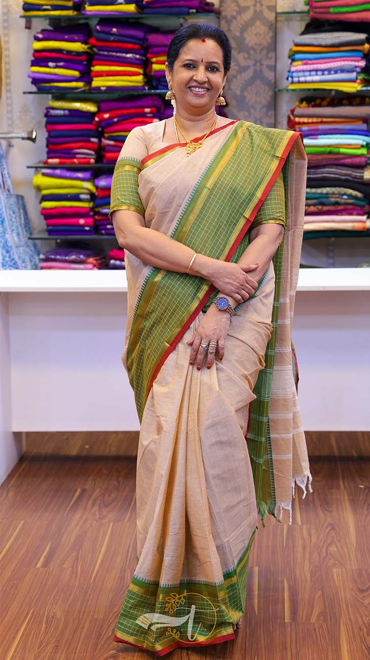 Woman wearing a traditional saree in a store setting with colorful fabrics in the background.