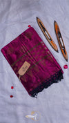 Magenta scarf with black patterns and a brand tag, accompanied by three wooden sticks on a light gray background.