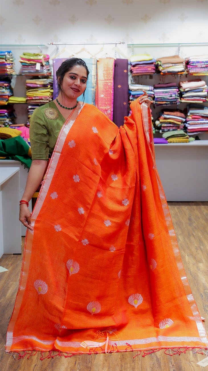 Woman holding an orange saree with a pattern in a fabric store.