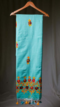 Turquoise scarf with floral embroidery and tassels on a hanger against a dark background