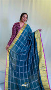 Woman wearing a blue saree with a gold border against a white background