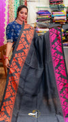 Woman holding a dark gray saree with red and pink patterns in a fabric store.