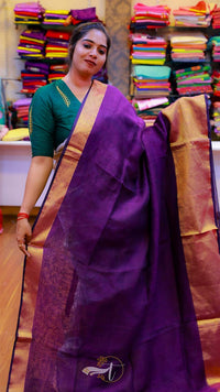 Woman wearing a purple saree with a green blouse in a fabric store.