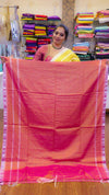 Woman holding a pink saree in a store setting with colorful fabrics in the background.