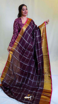 Woman wearing a traditional saree with a checkered pattern and gold border on a plain background