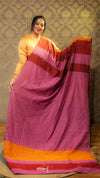 Woman holding a pink saree with orange and red border against a patterned wall.