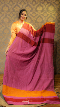 Woman holding a pink saree with orange and red border against a patterned wall.