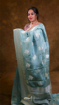 Woman wearing a light blue saree with white patterns against a brown background