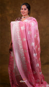 Woman wearing a pink saree with white floral patterns on a brown background