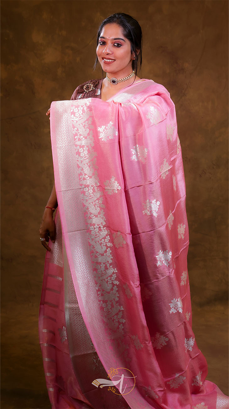 Woman wearing a pink saree with white floral patterns on a brown background