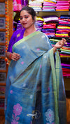 Woman wearing a blue saree with floral patterns in a colorful fabric store.
