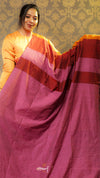 Woman holding a maroon saree with an orange blouse against a patterned wall.