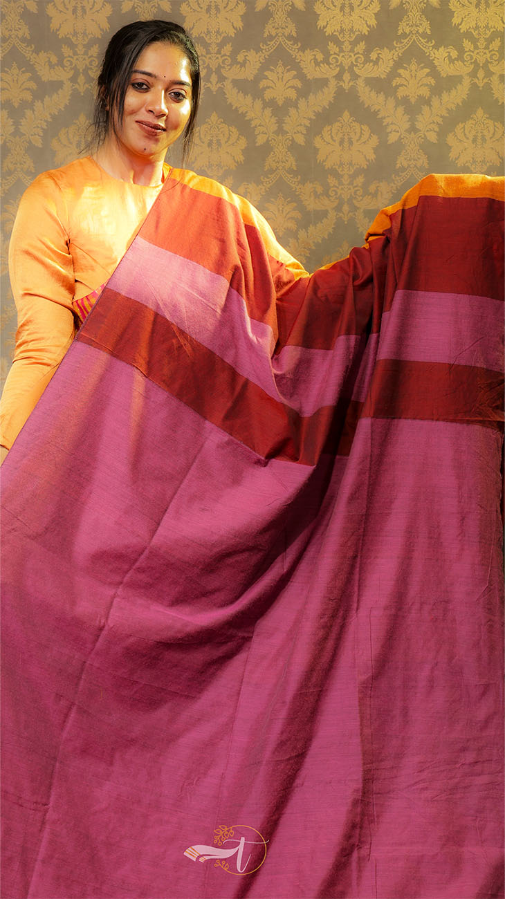 Woman holding a maroon saree with an orange blouse against a patterned wall.
