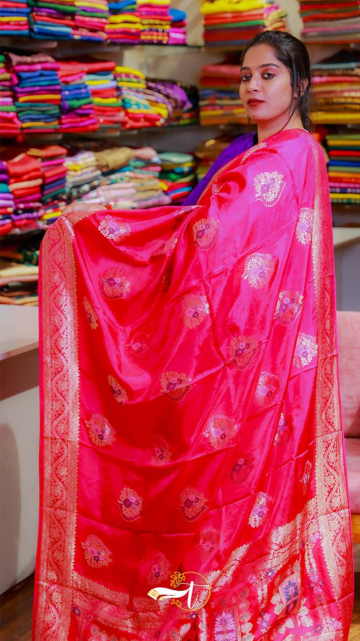 Woman wearing a bright pink saree with gold patterns in a fabric store.