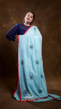 Woman wearing a light blue saree with black eye patterns on a brown background